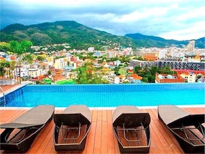 A swimming pool with lounge chairs, a view of a cityscape with buildings and mountains in the background. - Bliss Patong 2 bedrooms Apartment (Patong)