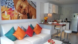 A modern living room with a white sofa, colorful cushions, a coffee table with a vase of flowers, and a large Buddha painting on the wall.