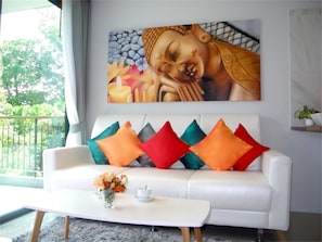 A white sofa with colorful cushions, a vase of flowers, and a Buddha painting on the wall.