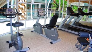 A gym with cardio machines, a bench, and large windows offering views of the outside.