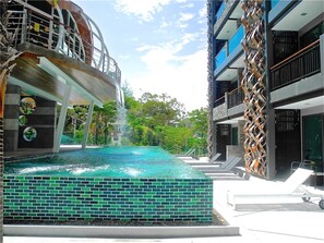 A swimming pool with a waterfall feature, surrounded by modern buildings with balconies and outdoor seating areas.