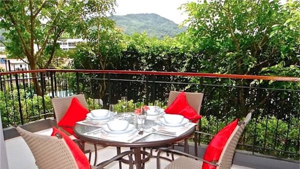 A round table with four chairs, each with a red cushion, set outdoors with a view of greenery and hills in the background. - Emerald Patong 1 bedroom Modern Apartment (Patong)
