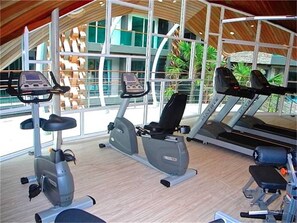 A gym with cardio machines, benches, and a large window offering a view of the outside.