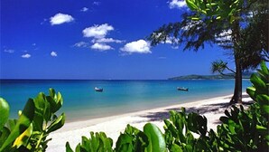 A beach with clear turquoise water, a sandy shore, and a few boats. - Emerald Patong 1 bedroom Modern Apartment (Patong)