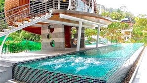 A swimming pool with a circular structure adjacent to it, a staircase leading to a covered area, and a view of surrounding greenery. - Emerald Patong 1 bedroom Modern Apartment (Patong)