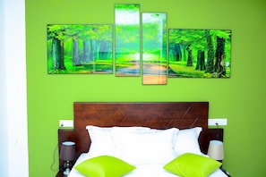 A hotel room with a green wall, a bed with white and green pillows, and a large forest-themed artwork above the bed. - Mama Beach Villa (Negombo)