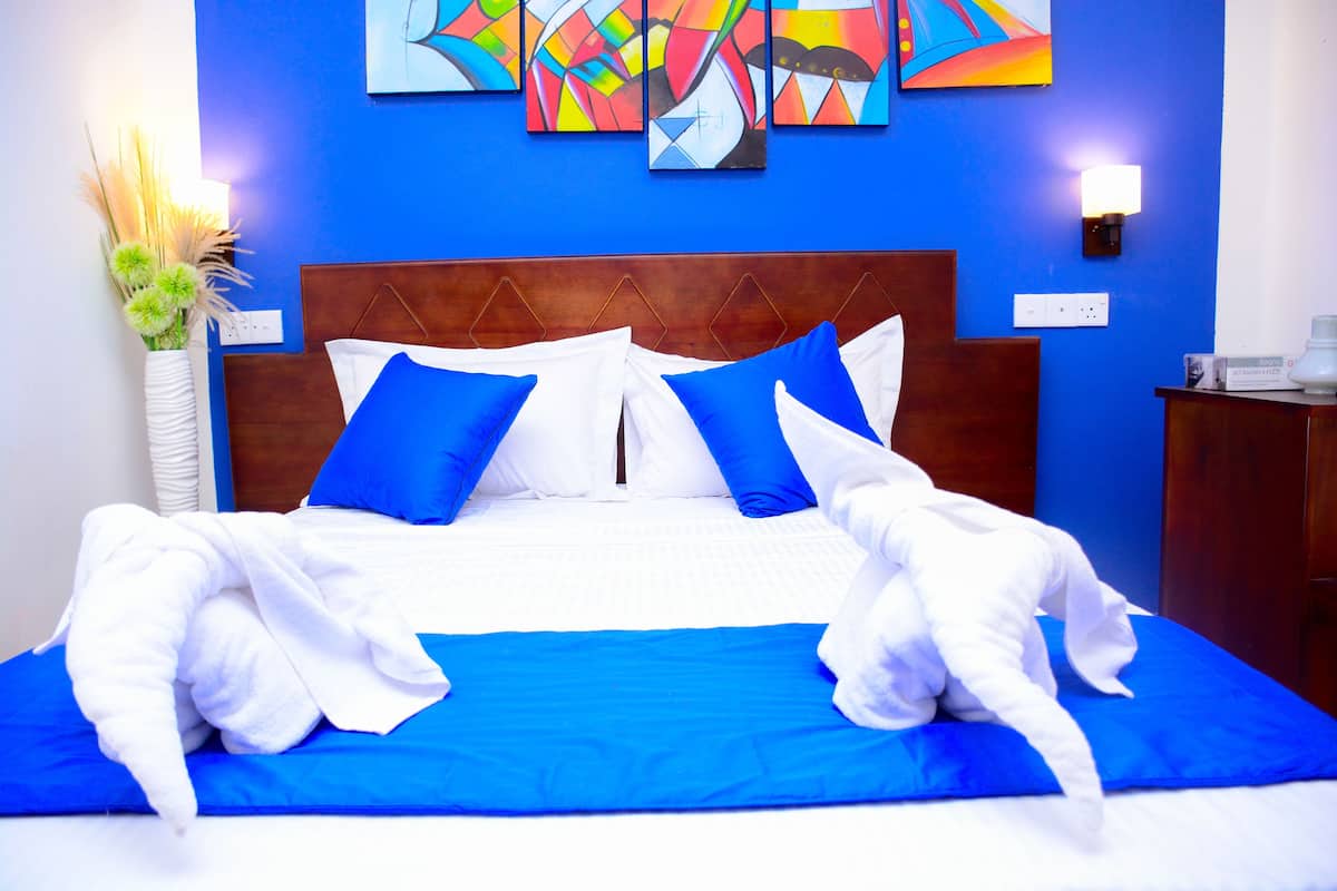 A neatly made bed with blue and white bedding, a wooden headboard, and colorful abstract paintings on the wall.