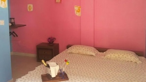 Una camera da letto con un letto, cuscini, un comodino e un tavolino con una bottiglia e fiori.