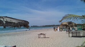 Una spiaggia con ombrelloni di paglia, un tavolo e una piccola costruzione, probabilmente una capanna da spiaggia.
