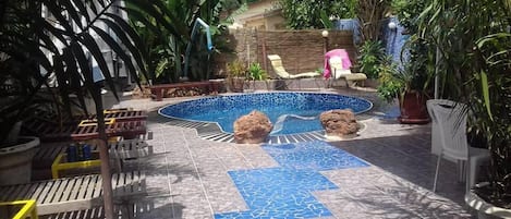 A pool area with a tiled floor, lounge chairs, and potted plants.
