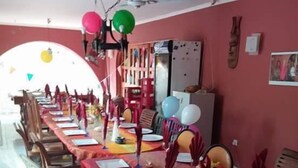 Zona pranzo con un lungo tavolo apparecchiato per più persone, sedie, ventilatori a soffitto e palloncini.