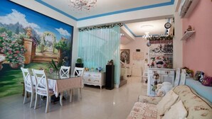 Una habitación con una mesa de comedor dispuesta para cuatro, un sofá, una araña y una pared decorada con un mural floral.