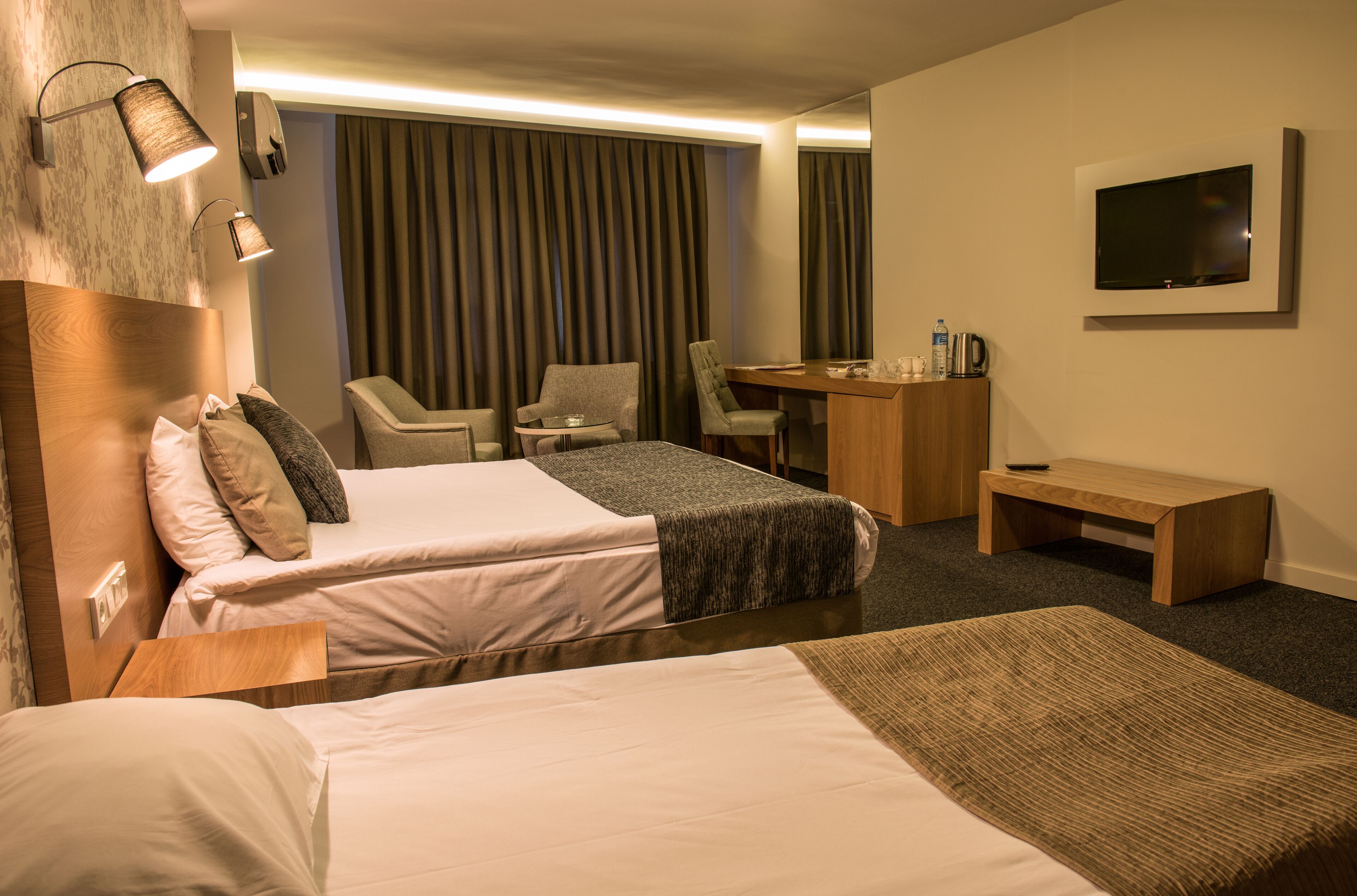 A hotel room with two beds, a desk, a chair, a TV, and a minibar.