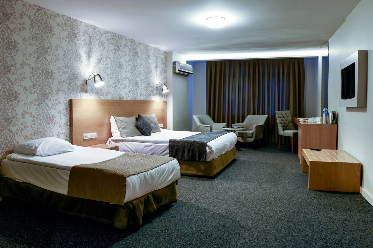 A hotel room with two beds, a desk, a chair, and a TV.