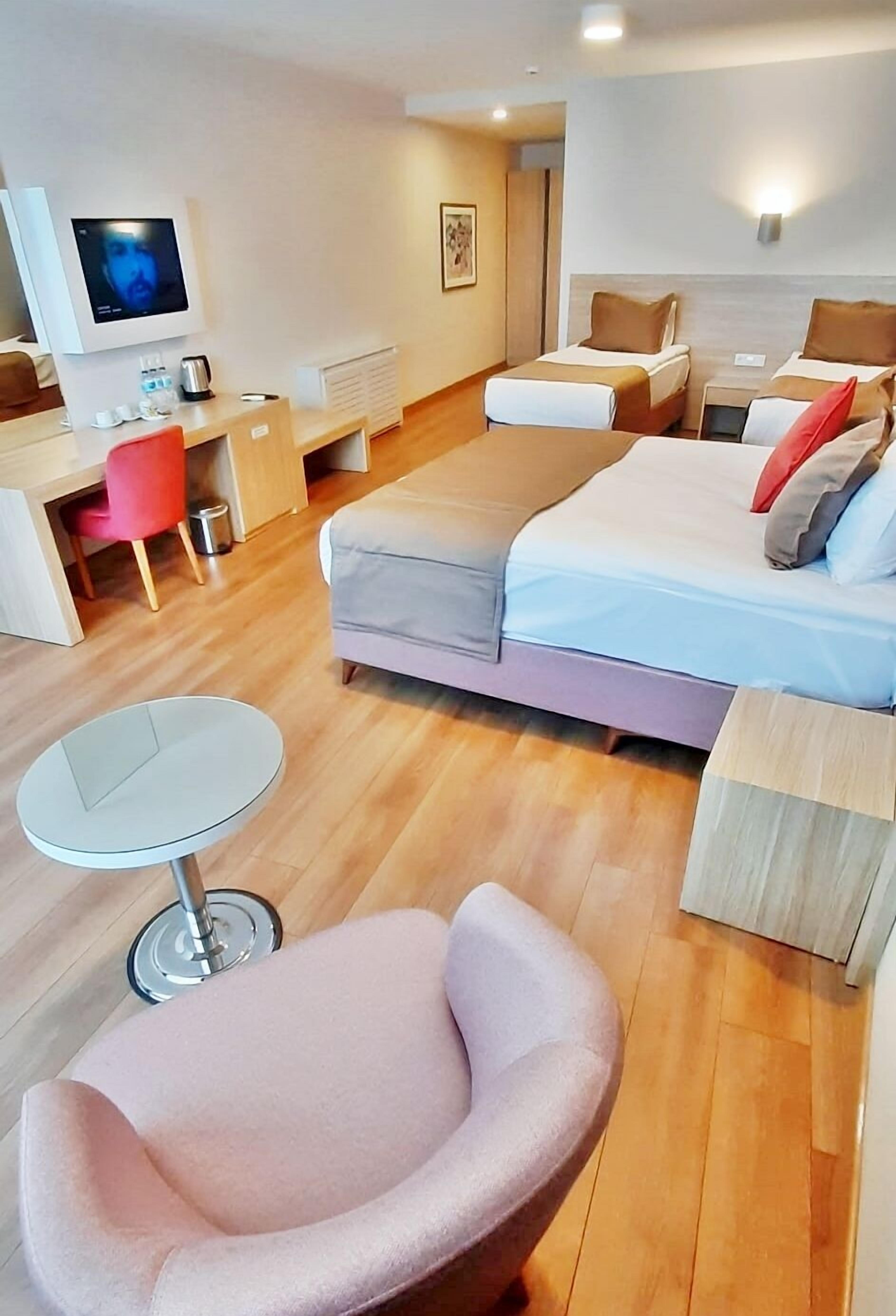 A modern hotel room with a bed, bedside tables, a desk, a chair, and a TV.