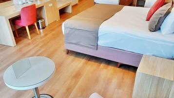 A modern hotel room with a bed, bedside tables, a desk, a chair, and a TV.