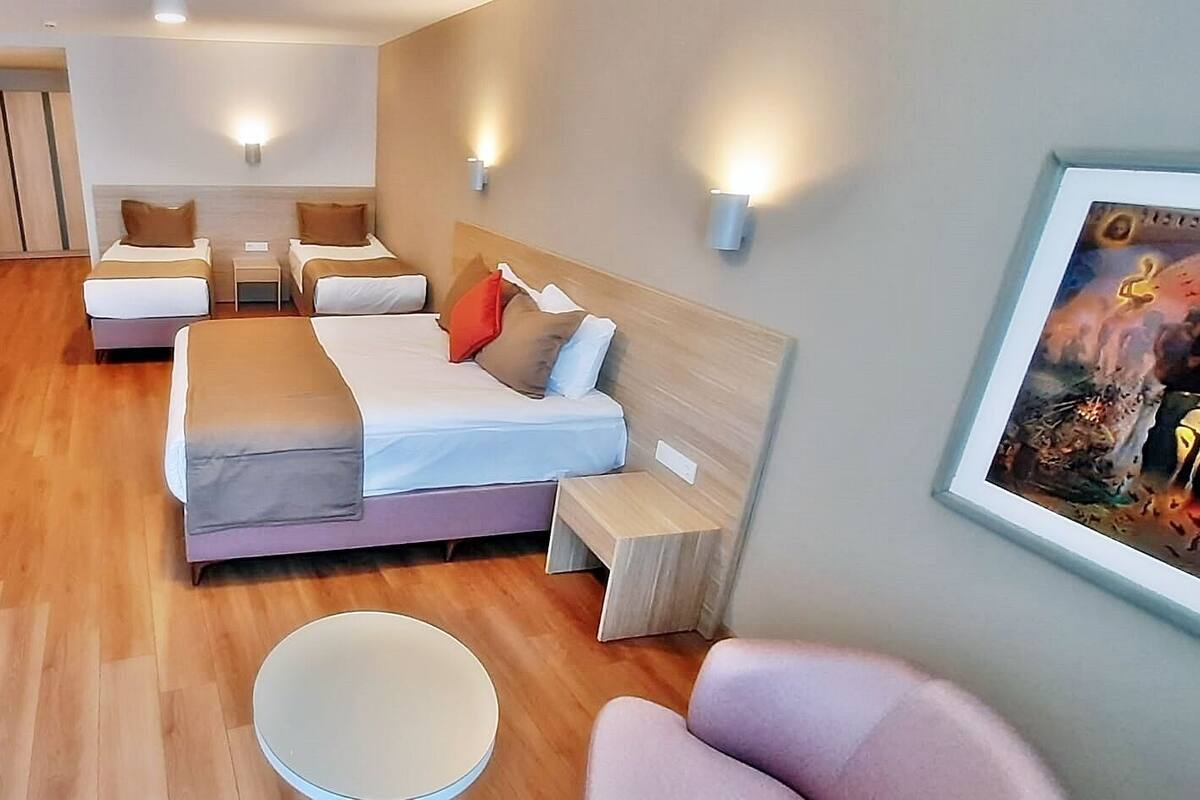 A hotel room with a large bed, a desk with a chair, a small round table, and a TV.
