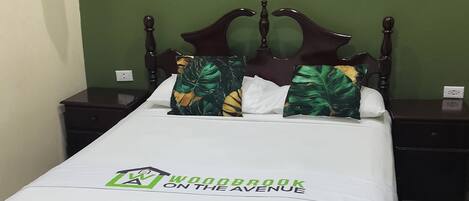 Una habitación de hotel con una cama, paredes verdes, un cuadro enmarcado y un perchero.