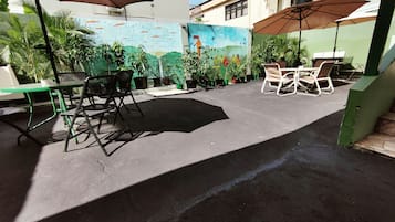 An outdoor patio area with tables and chairs, surrounded by potted plants and a mural on the wall.