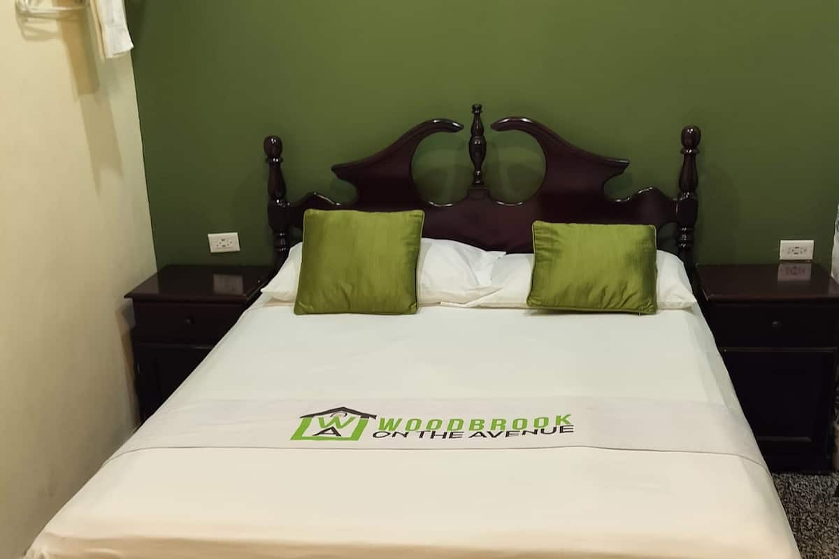A neatly made bed with a green and white bedspread, two green pillows, and a framed picture on the wall.