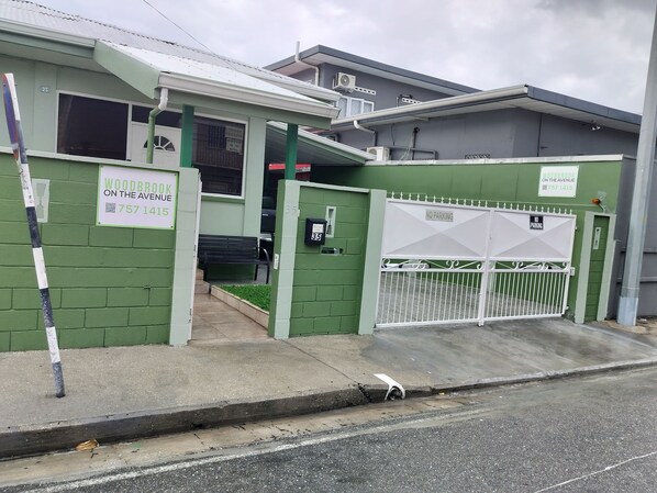 A building with a green facade, a gated entrance, and a bench outside. - Woodbrook on the Avenue (Port of Spain)