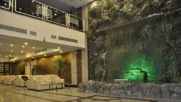Una hall d'albergo con area salotto, una parete in pietra con elemento d'acqua e un balcone con vista.