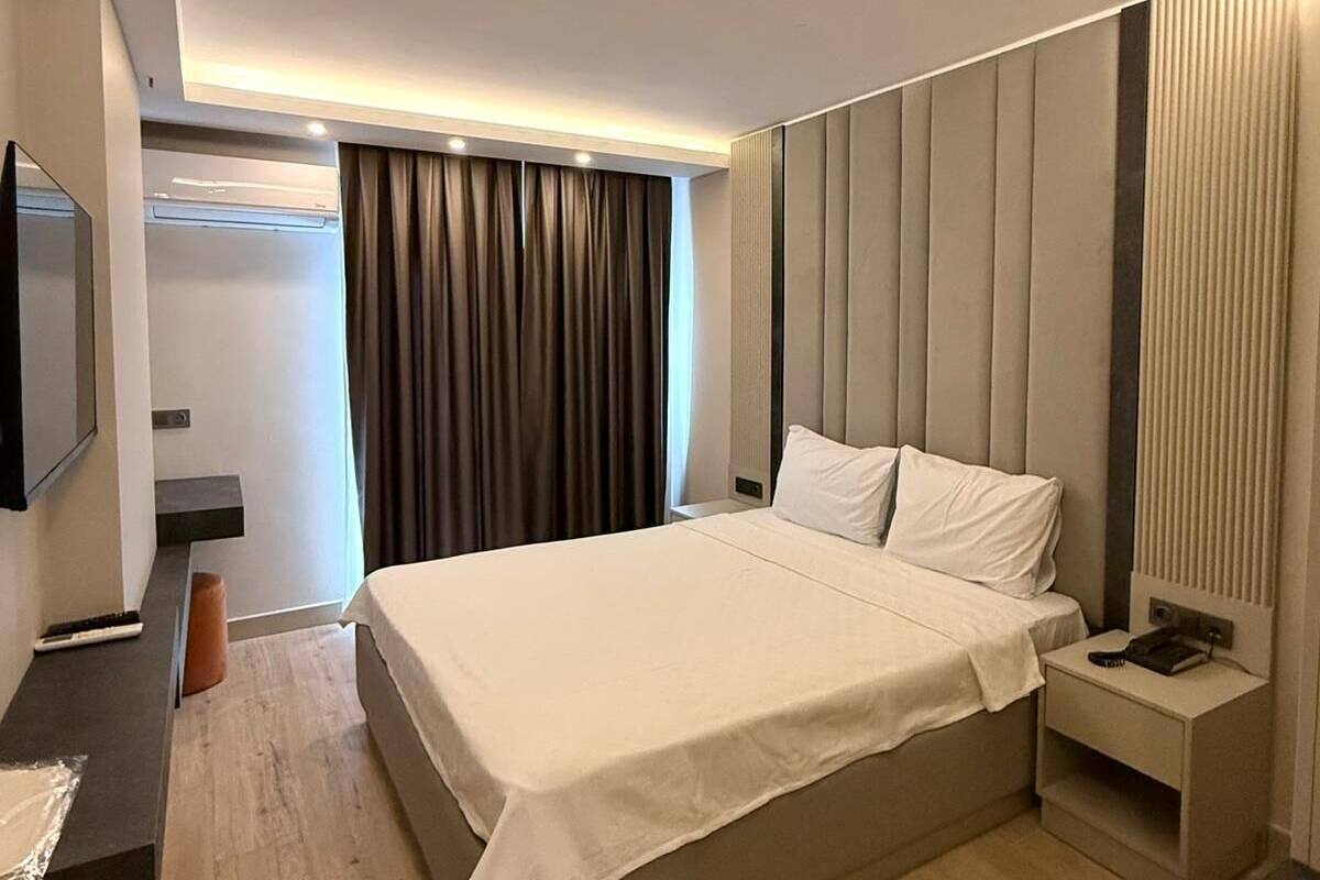 A modern hotel room with a large bed, bedside tables, a TV, and a built-in air conditioning unit.