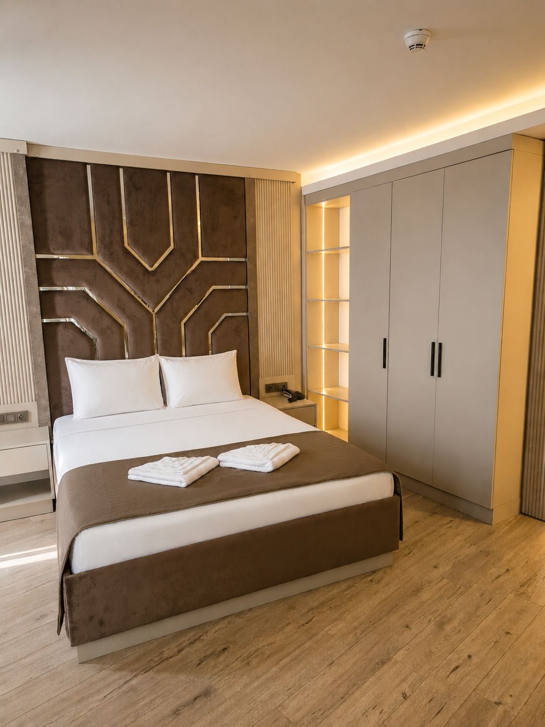 A modern hotel room with a large bed, a wardrobe, and a bedside table.