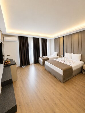A modern hotel room with a large bed, a smaller bed, a desk with a kettle, and a flat-screen TV. - Hotel Kayalar (Antalya)