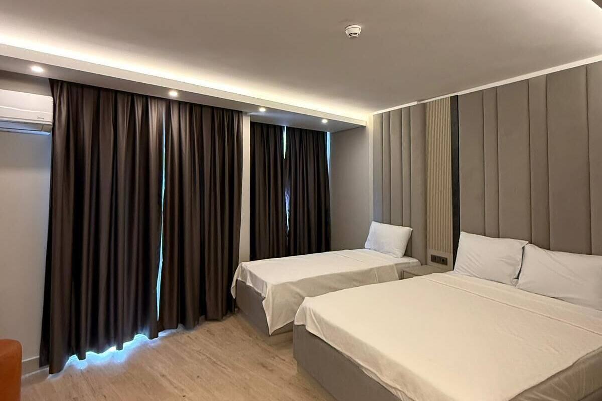 A modern hotel room with two beds, a large window with curtains, a ceiling light, and a wooden floor.