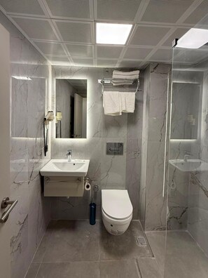 A bathroom with a marble sink, a toilet, and a glass-enclosed shower. - Hotel Kayalar (Antalya)