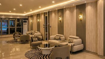 A spacious, well-lit lounge area with a modern design, featuring a central seating arrangement and a large mirror.