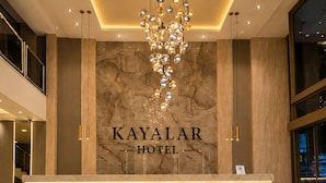 A reception desk with 'KAYALAR HOTEL' signage, a modern chandelier, and a marble wall. - Hotel Kayalar (Antalya)