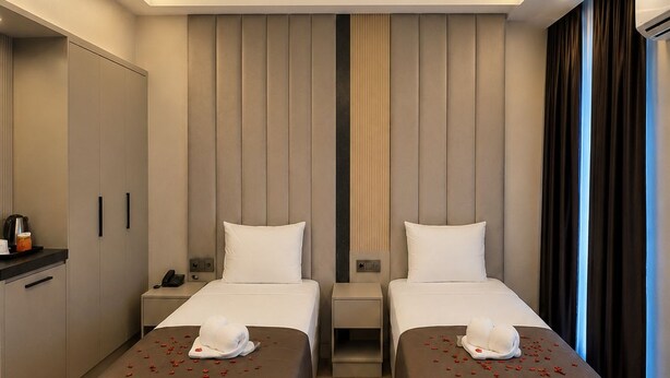 A hotel room with two beds, a desk, a wardrobe, and a view of the city. - Hotel Kayalar (Antalya)