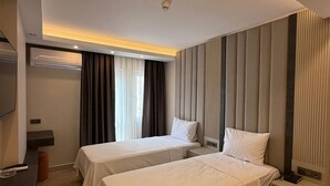 Una camera d'albergo con due letti, una televisione a schermo piatto, una scrivania e una finestra con tende.