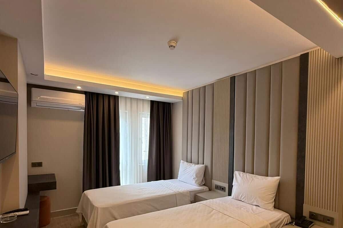 A hotel room with two beds, a flat-screen TV, a desk, and a window with curtains.