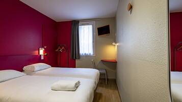 A hotel room with two beds, a desk, a chair, a TV, and a window with curtains.