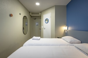 Habitación de hotel con dos camas, un espejo, una puerta y una lámpara fijada a la pared.