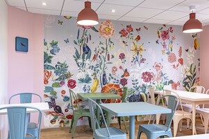 Un rincón de comedor con arte floral de colores en la pared, sillas verdes y azules, y una mesa blanca.