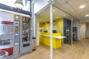 Un espacio interior moderno con una máquina expendedora, una barra amarillo brillante y una exhibición de bebidas.