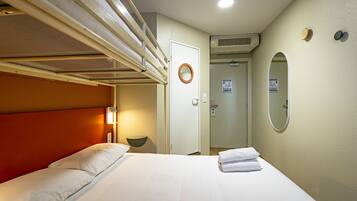 A hotel room with a bunk bed, a bedside lamp, a round mirror, and a bathroom door.