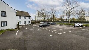 A parking lot with several cars, a white building with multiple windows, and leafless trees. - Vinihôtel (Beaune)