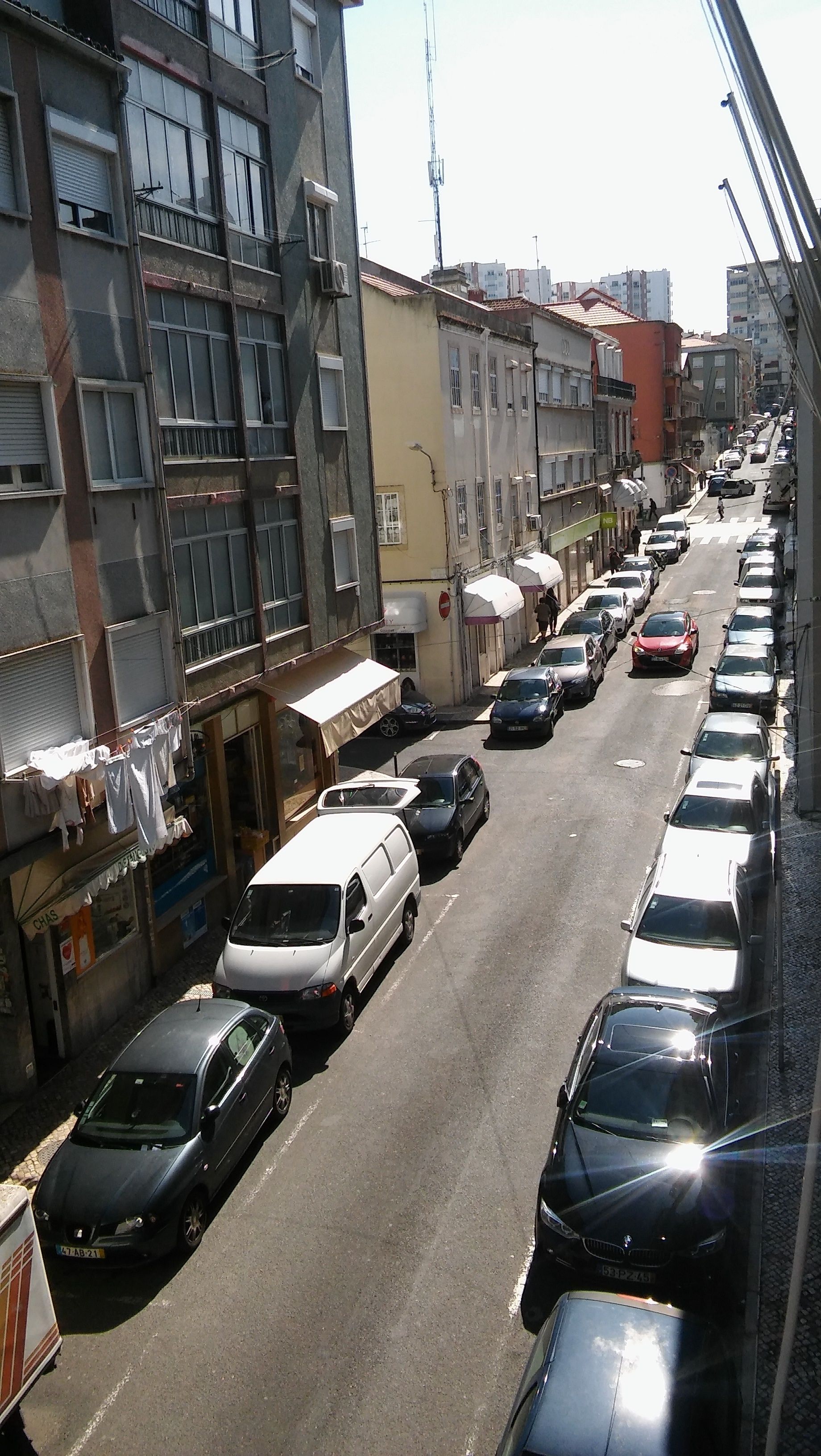 A narrow urban street lined with parked cars and multi-story buildings.