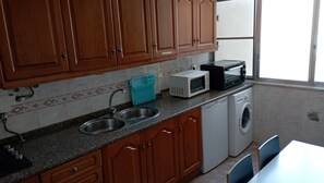 A kitchen with wooden cabinets, a double sink, a microwave, a toaster, and a washing machine. - Oriente DNA Studios II (Loures)