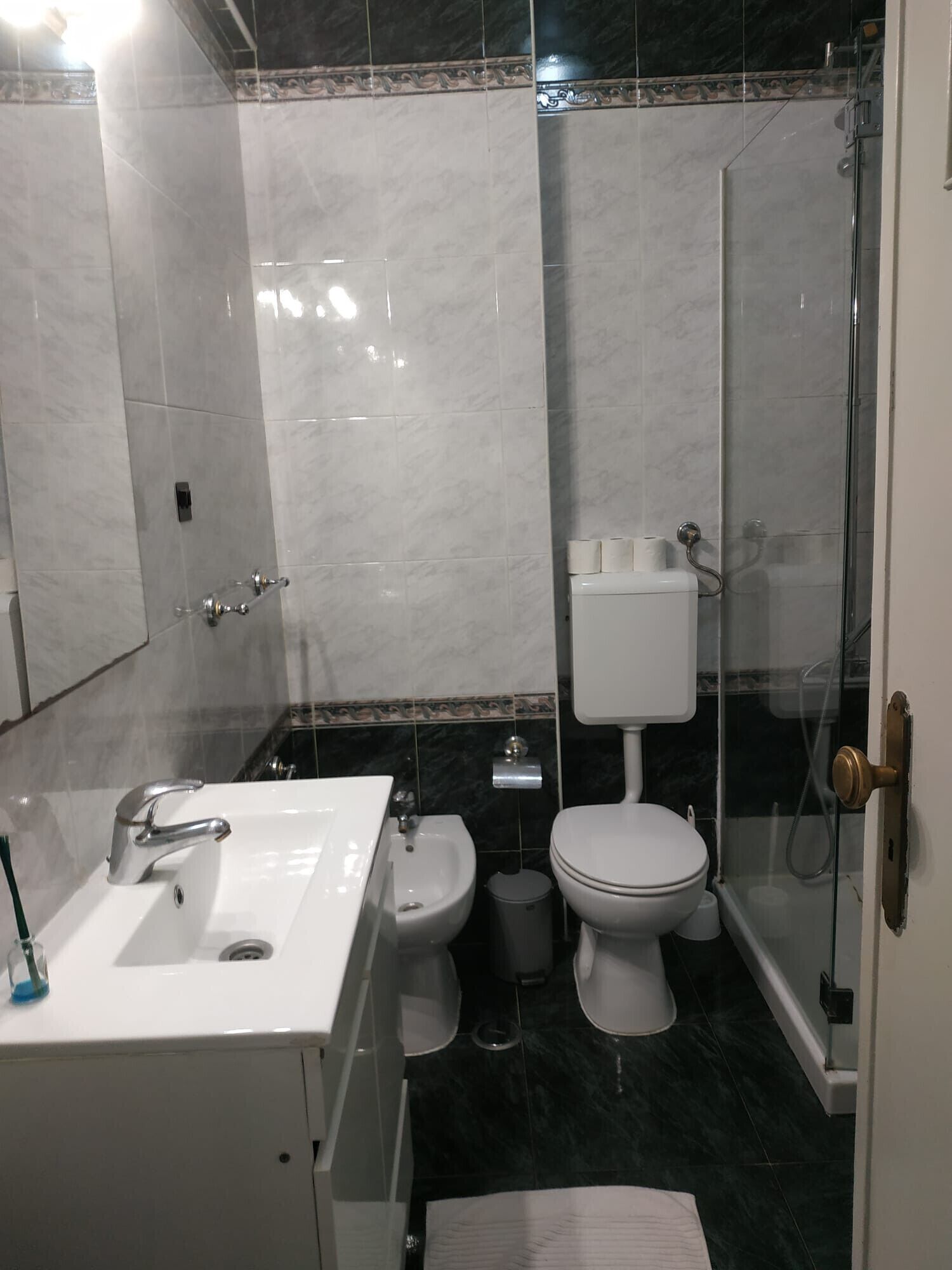 Een badkamer met een wastafel, bidet, toilet en een douche met glazen wanden.
