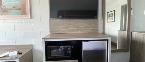 A compact kitchenette with a microwave, refrigerator, and a small cabinet. A flat-screen TV is mounted above the counter.