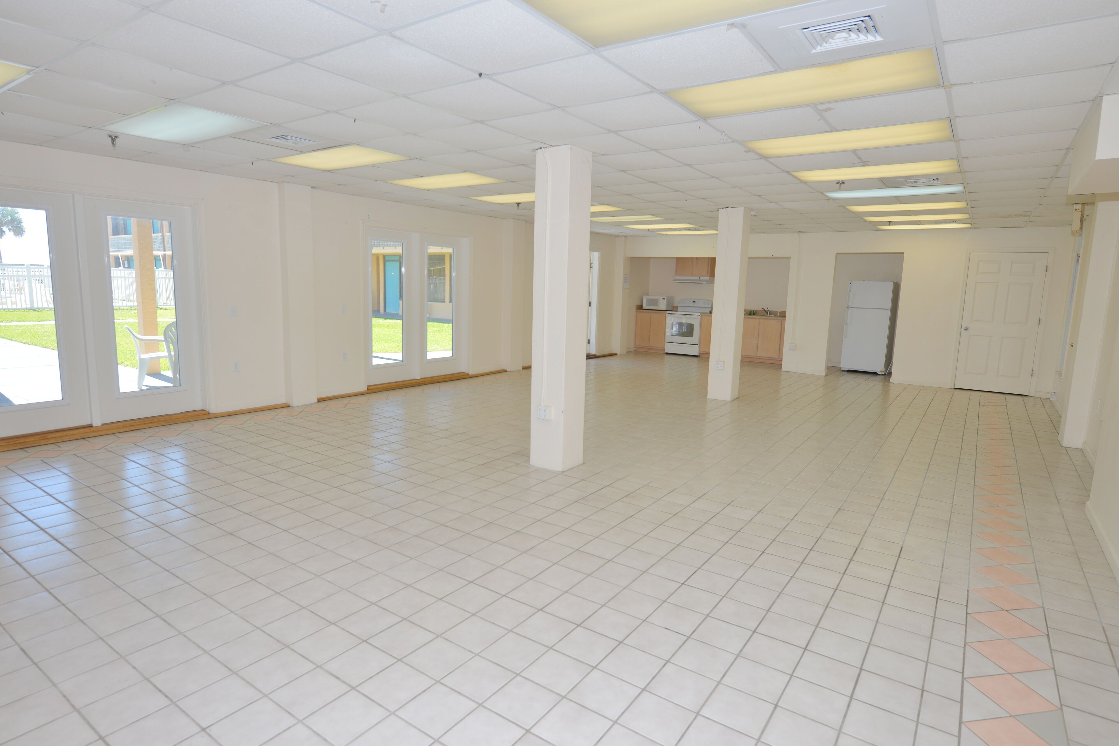 Een ruime, lege kamer met witte betegelde vloeren en een hoog plafond met fluorescent verlichting.