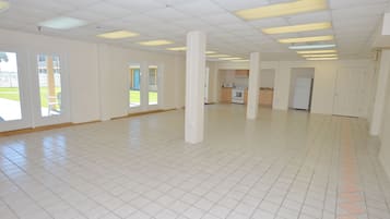 Een ruime, lege kamer met witte betegelde vloeren en een hoog plafond met fluorescent verlichting.