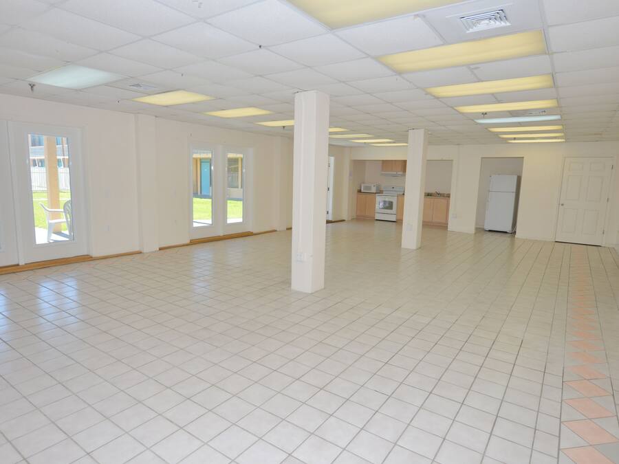 Een ruime, lege kamer met witte betegelde vloeren en een hoog plafond met fluorescent verlichting.