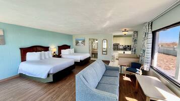 A hotel room with two beds, a sofa, a dining table, and a view of the beach.